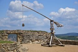 Photo of a reconstructed medieval trebuchet on a stone platform against a cloudy sky in the background