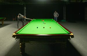 A player taking a shot at a practice snooker table, photographed from the opposite end of the table using a low camera angle to give forced perspective