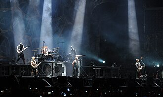 Rammstein performing at Wacken Open Air in August 2013; upper level (left to right): Oliver Riedel, Christoph Schneider, and Christian Lorenz; lower level (left to right): Paul Landers, Till Lindemann, and Richard Kruspe