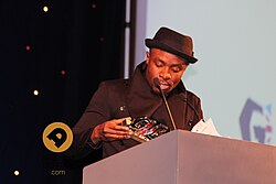 Man accepting award, wearing black hat and top.