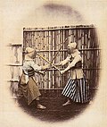 Kendō fight with bamboo shinai, in the background a bamboo fence