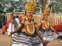 Two colourfully-dressed dancers with spears, masks and headdresses