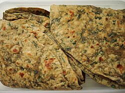 A stack of parathas that have a large amount of herbs mixed baked into the dough