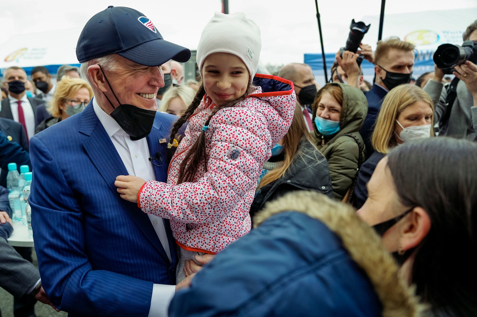 Photo of a smiling Biden holding a child, with a mask lowered onto his chin